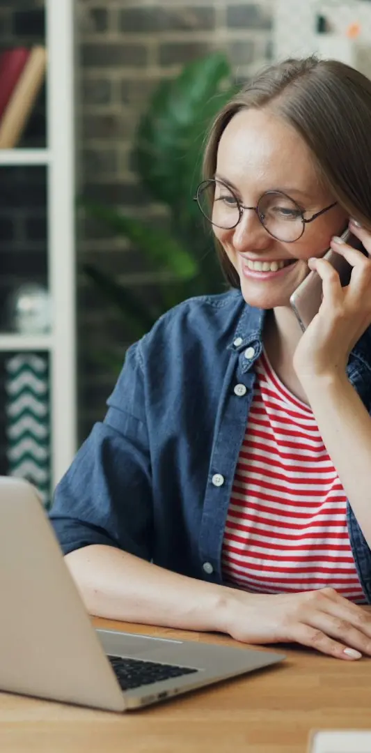 a woman talking on a cell phone while using a laptop